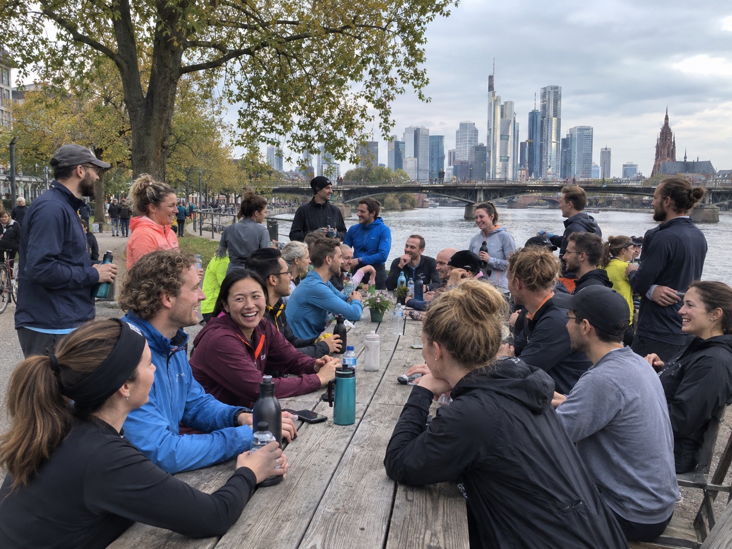 Eine große Laufgruppe nach der gemeinsamen Runde an einem langen Tisch am Main